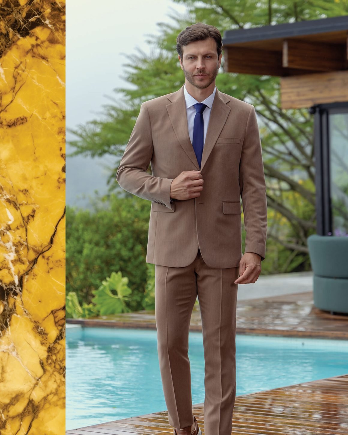 Terno taupe à beira de piscina, com casa de vidro ao fundo